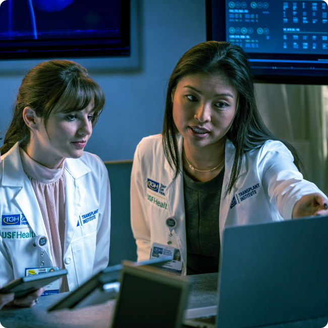 femle clinical professional points to a monitor to show something to her female colleague in a medical setting