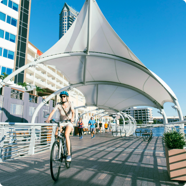 female riding a bicycle with walkers and joggers behind her on the tampa riverwalk, located in tmrd
